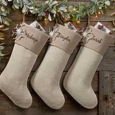 three christmas stockings hanging on a wooden wall with greenery and lights in the background