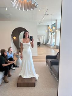 a woman in a white wedding dress taking a photo with her cell phone while others look on