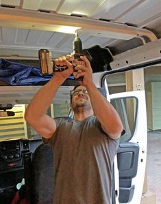 a man holding up a beer bottle in front of his face while standing next to a van