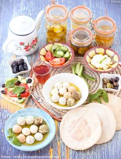 a table topped with plates and bowls filled with different types of food next to jars of pickles