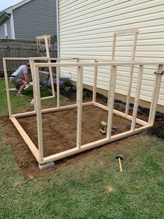 a man is digging in the ground next to a house with a wooden frame on it