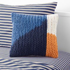 a blue and white pillow sitting on top of a bed next to a striped pillow