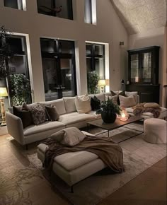 a living room filled with lots of furniture next to tall windows on top of a wooden floor