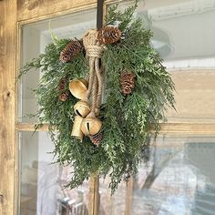 a wreath with bells and pine cones hangs on a door handle in front of a window