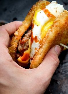 a hand holding a sandwich with meat, cheese and sauce on it's side