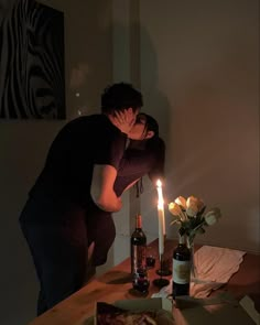 a man and woman kissing in front of a table with pizza, wine bottles and candles