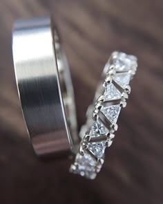 two wedding rings sitting on top of a wooden table next to each other with diamonds in them