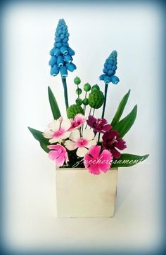 blue and pink flowers are in a white vase with green leaves on the top, against a white background