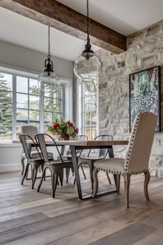 a dining room table and chairs in front of a stone wall with large glass windows