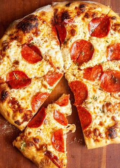 a pepperoni pizza cut into four slices on a wooden cutting board with one slice missing