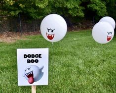 three balloons with faces on them are in the grass near a sign that says dodge boo