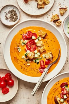 two bowls of soup with tomatoes, cucumbers and croutons on the side