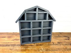 a gray shelf with shelves on top of it sitting on a wooden table next to a white wall