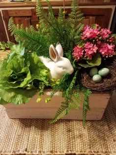 an arrangement of flowers and plants in a wooden box on a table with a white rabbit figurine