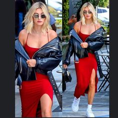 a woman in a red dress and leather jacket walking down the street with her hand on her hip