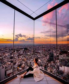 a woman sitting on top of a building looking out over the city at sunset or dawn