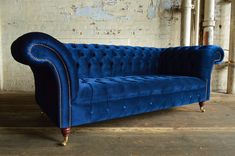 a blue couch sitting in front of a brick wall with exposed piping on it