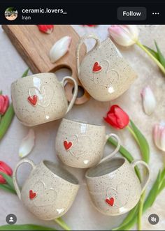 four cups with hearts painted on them sitting next to tulips and a cutting board