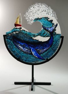 a glass sculpture with a sailboat and a whale on it's back in front of a wave