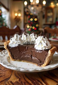 a chocolate pie with whipped cream on top sits on a plate in front of a christmas tree