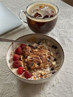 a bowl of oatmeal with raspberries next to a cup of coffee