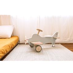 a wooden toy airplane sitting on top of a rug in front of a bed with pillows