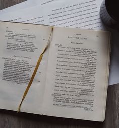 an open book sitting on top of a wooden table next to a cup and pen