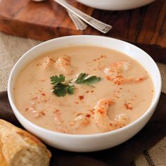 a bowl of soup with shrimp and parsley garnish on top, next to a piece of bread