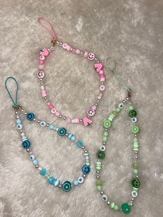 three necklaces with beads and charms on a white carpeted surface, one has a pink bow