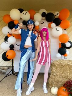 two people standing in front of a backdrop with balloons and pumpkins for halloween party