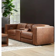 a brown leather couch sitting on top of a wooden floor next to a potted plant