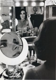 a black and white photo of a woman brushing her teeth in front of a mirror