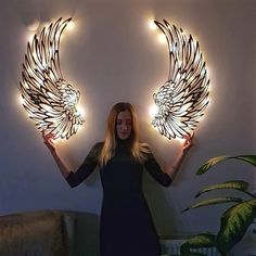 a woman standing in front of two angel wings with lights on the wall behind her