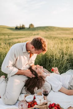 a man and woman laying on the grass with strawberries in their hands, kissing