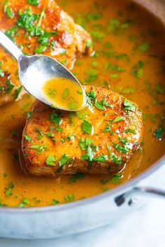 two pieces of meat are being spooned into a pot of soup with parsley on top