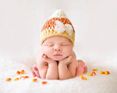 a newborn baby wearing a crochet hat laying on his side with corn kernels all around him