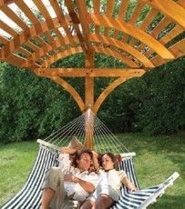 two women sitting in a hammock under a wooden structure with an attached canopy