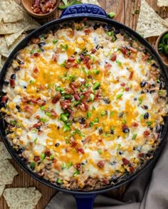 a skillet filled with cheese, black olives and green onions next to tortilla chips