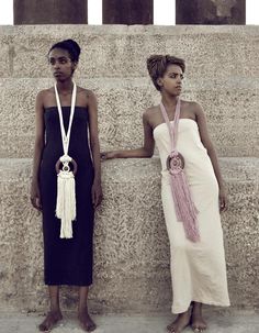 two women standing next to each other with necklaces on their necks and one wearing a black dress