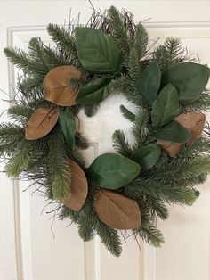 a wreath is hanging on the door with green leaves and greenery in front of it