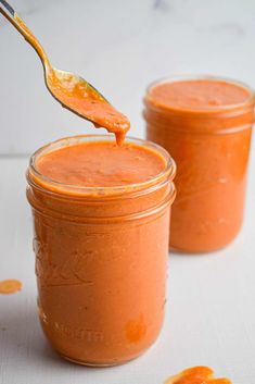 a spoon full of orange colored sauce on top of a white table with two jars