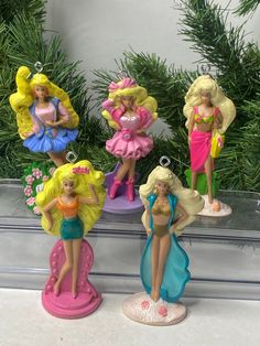 four barbie dolls sitting on top of each other in front of some christmas trees and pine branches