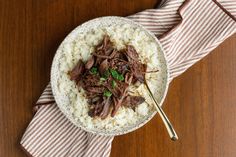 a bowl filled with rice and beef on top of a wooden table next to a striped napkin