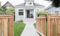 a small white house with a black and white dog on the front door way, behind a wooden fence