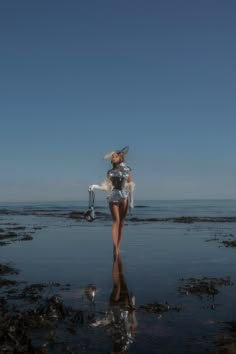 a woman standing on top of a sandy beach next to the ocean wearing a silver dress