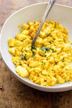 a white bowl filled with scrambled eggs on top of a wooden table