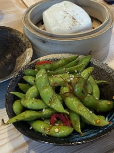 a bowl filled with green beans on top of a wooden table next to other bowls