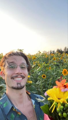 a man standing in the middle of a field with sunflowers and other flowers