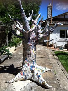 a tree that has been made out of newspaper strips and magazines is sitting on the sidewalk