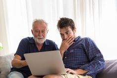 two people sitting on a couch looking at a laptop